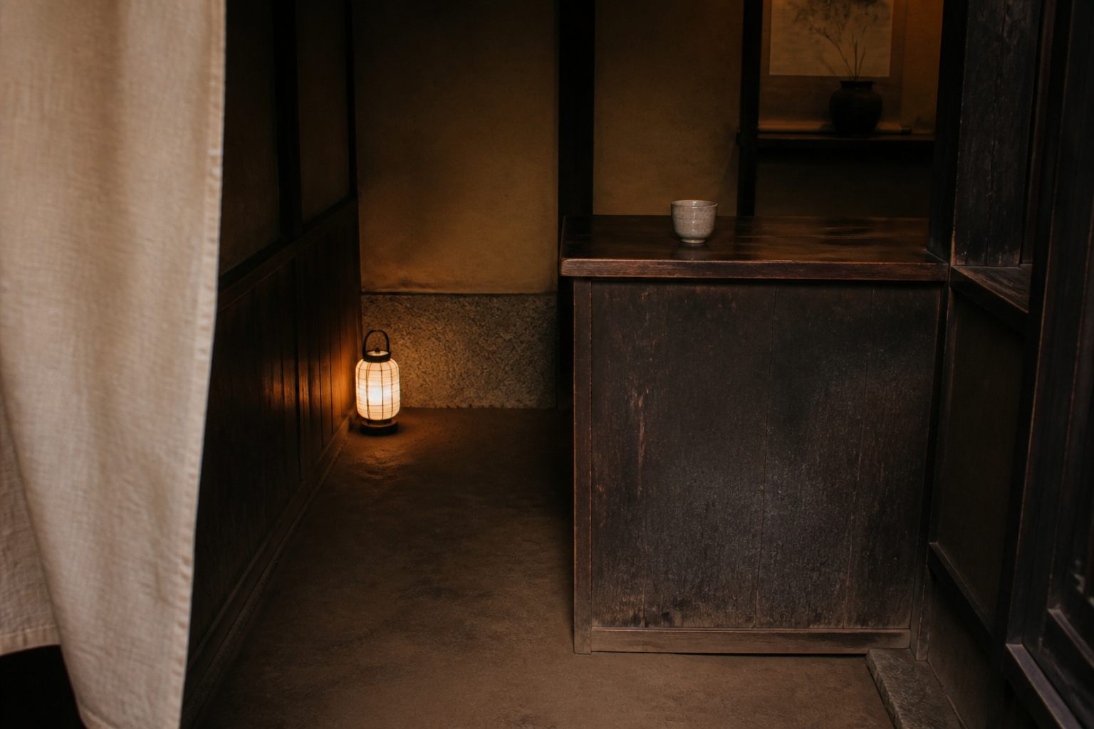 Inside the entrance: an earthen floor, a small lantern, and a single cup of tea set on a dark wooden counter.