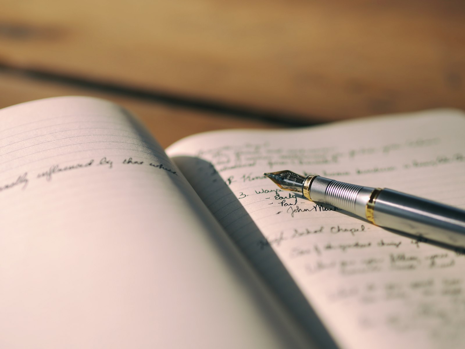 開かれた手帳に手書きの文字が並び、その上に万年筆が置かれている。